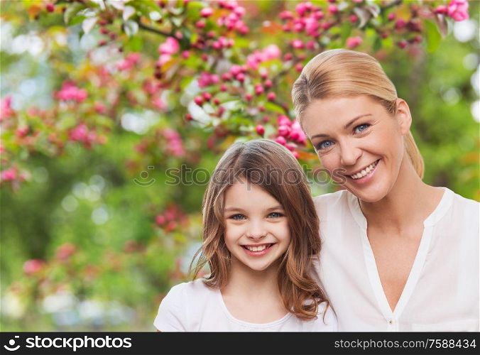 family, motherhood and people concept - happy smiling mother and daughter over cherry blossom background. happy mother and daughter over garden
