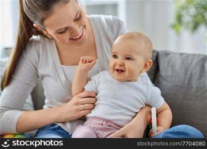 family, motherhood and people concept - happy smiling mother and little baby playing with rattle at home. mother and little baby playing with rattle at home