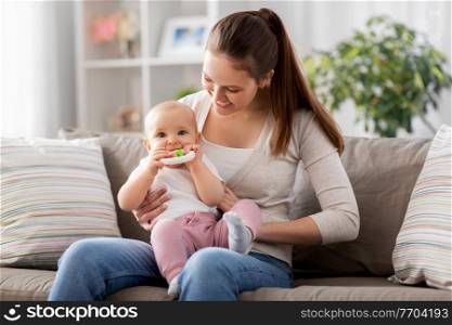 family, motherhood and people concept - happy smiling mother and little baby playing with teething toy or rattle at home. mother and little baby with teething toy at home