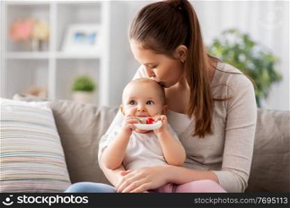 family, motherhood and people concept - happy smiling mother kissing little baby playing with teething toy or rattle at home. mother kissing baby with teething toy at home