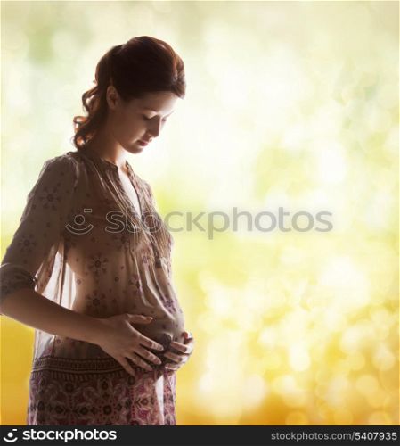 family, motherhood and pregnancy concept - silhouette backlight picture of pregnant beautiful woman touching her belly