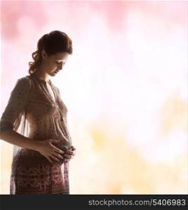 family, motherhood and pregnancy concept - silhouette backlight picture of pregnant beautiful woman touching her tummy