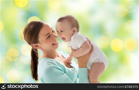 family, motherhood, child and parenthood concept - happy smiling young mother with little baby over green lights background