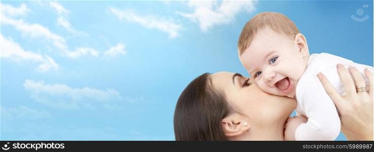 family, motherhood, children, parenthood and people concept - happy mother kissing her baby over blue sky and clouds background