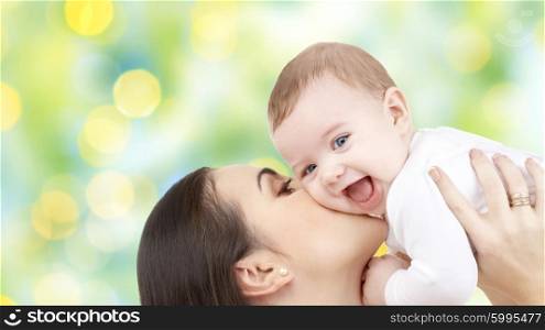 family, motherhood, children, parenthood and people concept - happy mother kissing her baby over green holidays lights background
