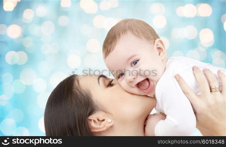 family, motherhood, children, parenthood and people concept - happy mother kissing her baby over blue holidays lights background