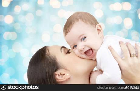 family, motherhood, children, parenthood and people concept - happy mother kissing her baby over blue holidays lights background