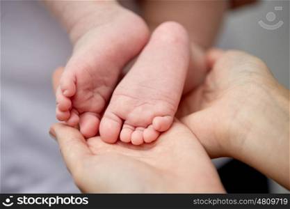 family, motherhood, parenting, people and child care concept - close up of newborn baby feet in mother hands