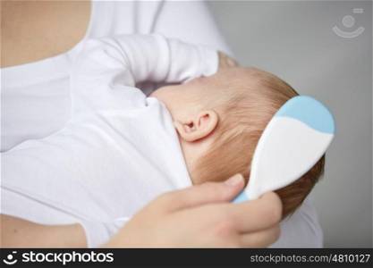 family, motherhood, parenting, people and child care concept - close up of mother with hairbrush brushing newborn baby hair