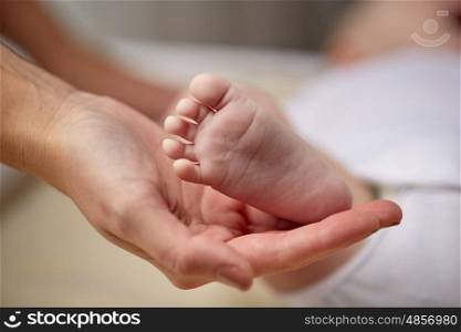 family, motherhood, parenting, people and child care concept - close up of newborn baby foot in mother hand