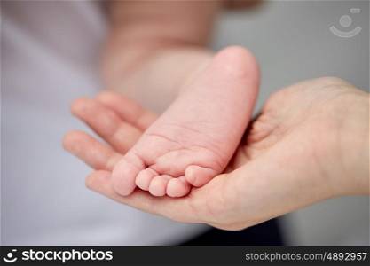 family, motherhood, parenting, people and child care concept - close up of newborn baby foot in mother hand