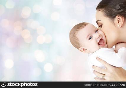 family, motherhood, parenting, people and child care concept - happy mother kissing adorable baby over blue holidays lights background