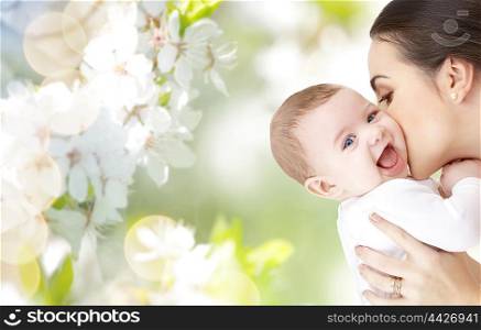 family, motherhood, parenting, people and child care concept - happy mother kissing adorable baby over green natural background