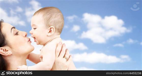 family, motherhood, parenting, people and child care concept - happy mother kissing adorable baby over blue sky background