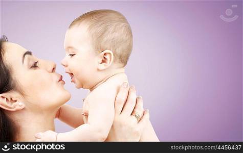 family, motherhood, parenting, people and child care concept - happy mother kissing adorable baby over violet background