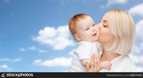 family, motherhood, parenting, people and child care concept - happy mother kissing adorable baby over blue sky background