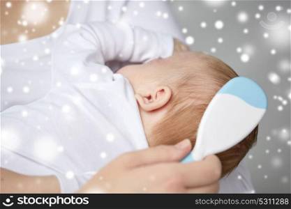 family, motherhood, people and child care concept - close up of mother with hairbrush brushing newborn baby hair over snow. close up of mother brushing newborn baby hair