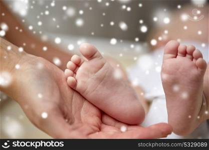 family, motherhood, people and child care concept - close up of newborn baby feet in mother hands over snow. close up of newborn baby feet in mother hands