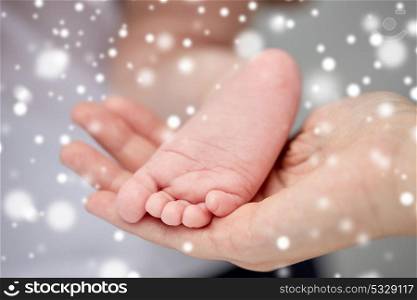 family, motherhood, people and child care concept - close up of newborn baby feet in mother hands over snow. close up of newborn baby feet in mother hands