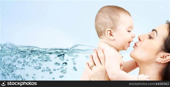 family, motherhood, people and child care concept - happy mother kissing adorable baby over blue background with water splash