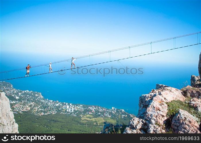 Family of brave father and kids on suspension bridge against the background of the sea and mountains. Family crossing the chasm on the rope bridge. Black sea background, Crimea, Russia