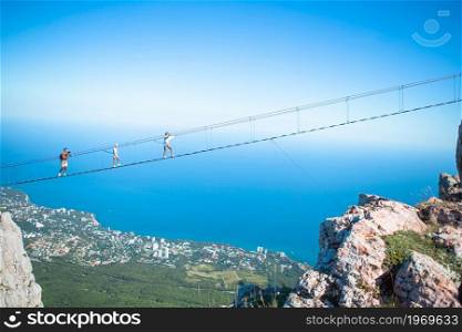 Family of brave father and kids on suspension bridge against the background of the sea and mountains. Family crossing the chasm on the rope bridge. Black sea background, Crimea, Russia