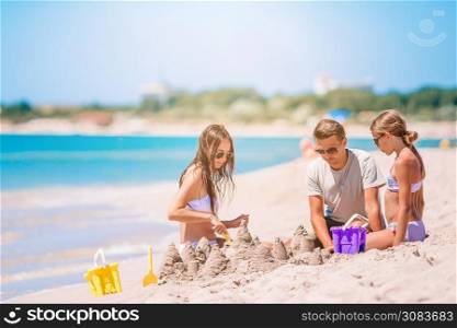 Family of dad and kids playing with sand on tropical beach. Father and kids making sand castle at tropical beach. Family playing with beach toys