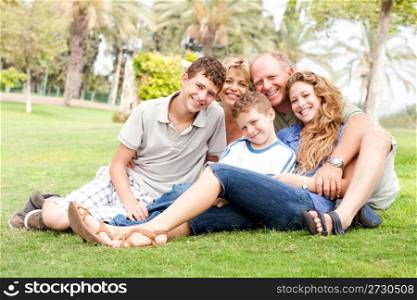 Family of five relaxing on sunny day in the park and smiling at camera