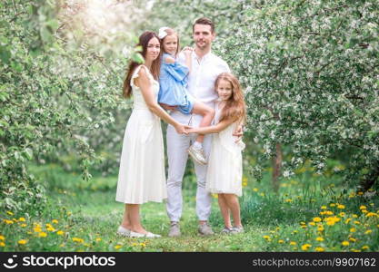 Family of four in blooming garden on beautiful spring day. Adorable family in blooming cherry garden on beautiful spring day