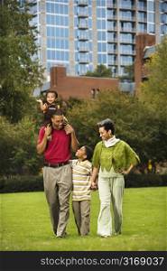 Family of four people walking in park smiling.