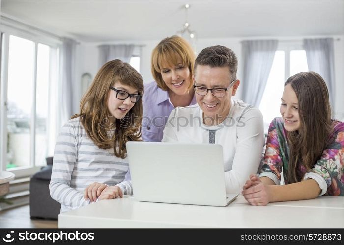 Family of four using laptop together at table in home