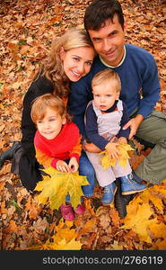 Family of four with yellow maple leaves in wood in autumn