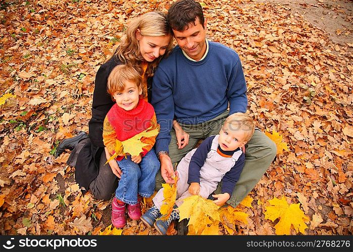 Family of four with yellow maple leaves in wood in autumn
