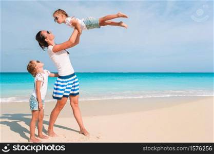 Family of mother and little daughters on the beach having fun. Adorable little girls and young mother on tropical white beach