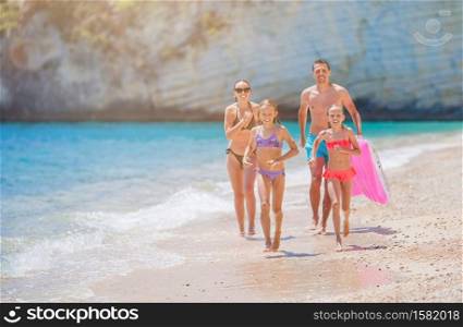Family of parents and children on the beach having fun. Kids and parents run on the seashore. Young family on vacation have a lot of fun