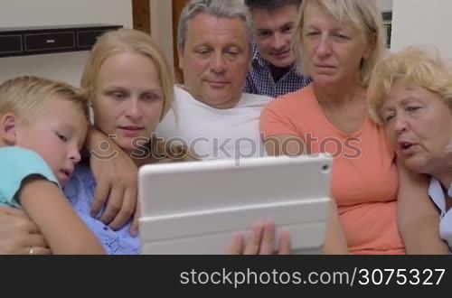 Family of parents, child and grandparents attracted to the touch pad. They watching entertaining video and laughing