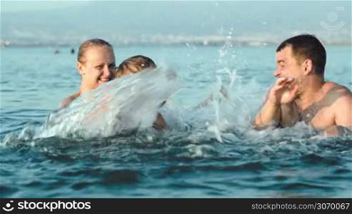 Family of three having fun in sea. Mother and son splashing water on father