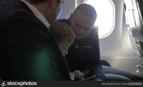 Family of three in the plane. Little boy playing on smartphone, parents watching him, mother giving prompts