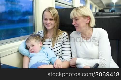 Family of three in the train. Mother and grandmother talking while boy watching cartoon on laptop