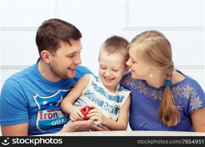Family of three is sitting at the table and playing. The father gives his son an apple.