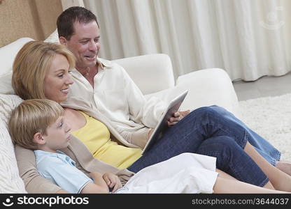 Family of three sit reading a digital book