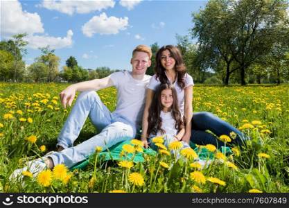 Family of three sitting on spring meadow of blooming yellow dandelion flowers being happy. Family on flower meadow