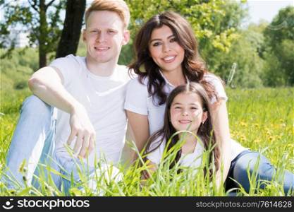 Family of three sitting on spring park meadow grass being happy. Family on park meadow