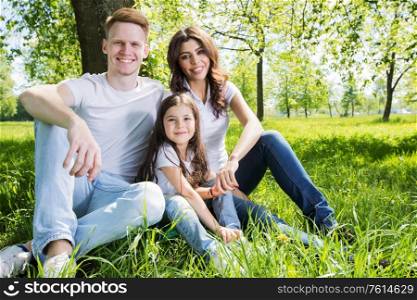 Family of three sitting on spring park meadow grass being happy. Family on park meadow