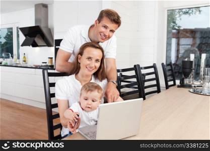 Family of three smiling with laptop at table