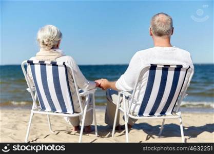 family, old age, travel, tourism and people concept - happy senior couple sitting on deck chairs on summer beach