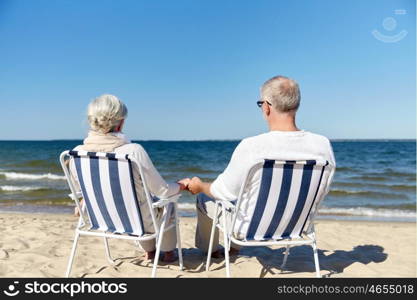 family, old age, travel, tourism and people concept - happy senior couple sitting on deck chairs on summer beach