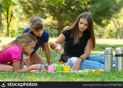 Family on a picnic, girl pours tea in glasses, children watch