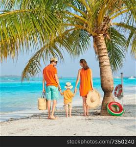 Family on beach, young couple in orange with three year old boy under the palm tree. Summer vacation at Maldives.