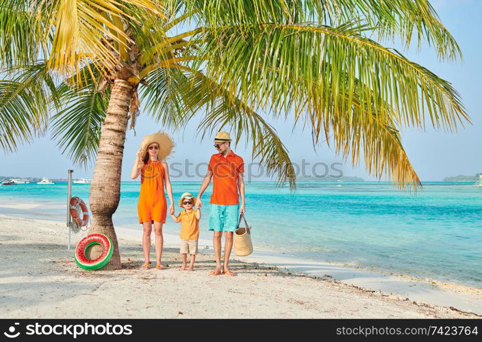 Family on beach, young couple in orange with three year old boy under the palm tree. Summer vacation at Maldives.